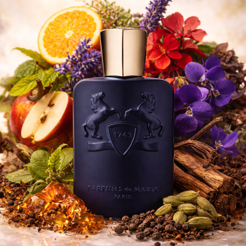 Blue perfume bottle with gold cap on a background of fruits, flowers, and spices